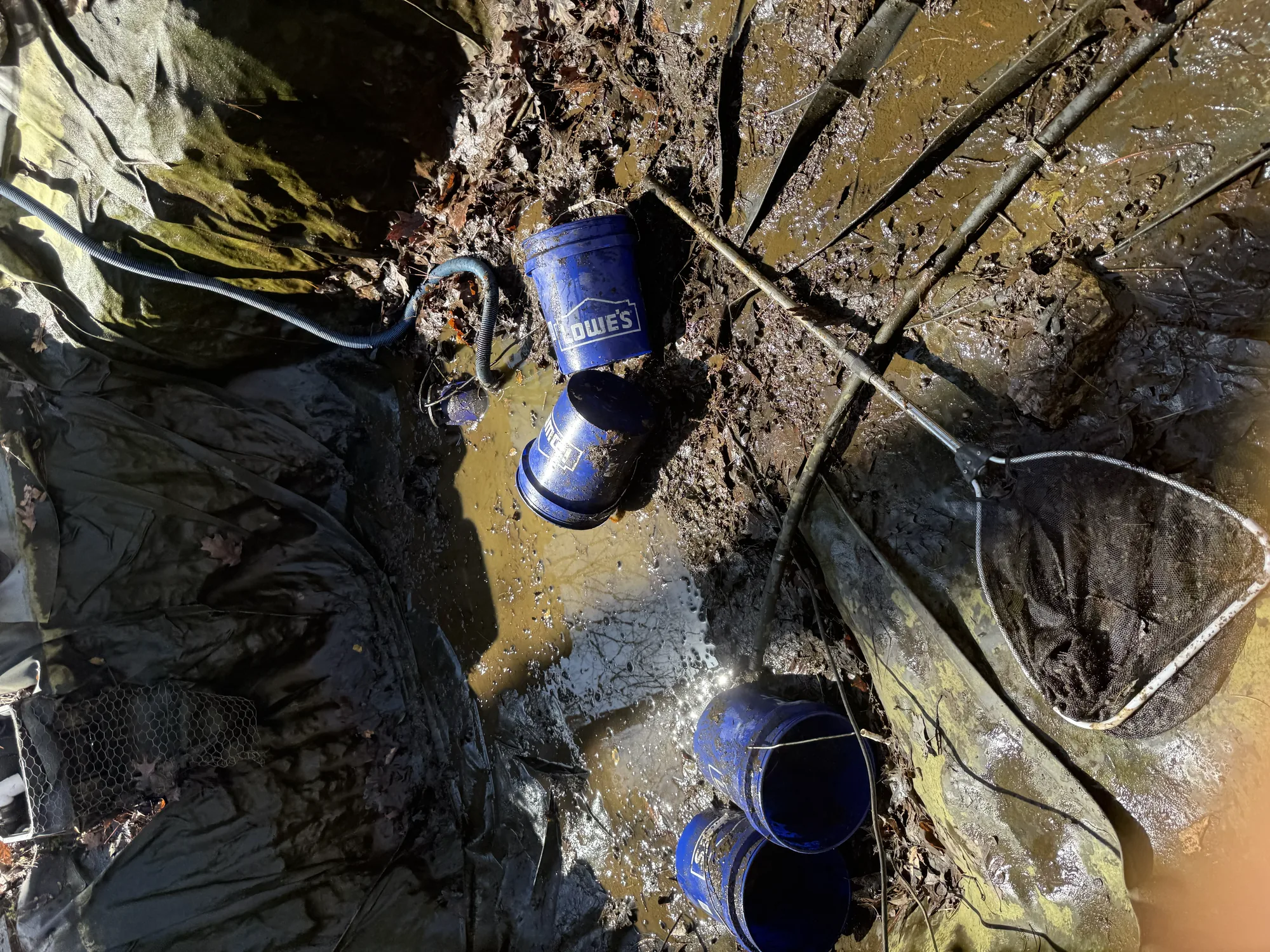 Pump plumbing and check valves exposed on the muddy floor of a drained pond