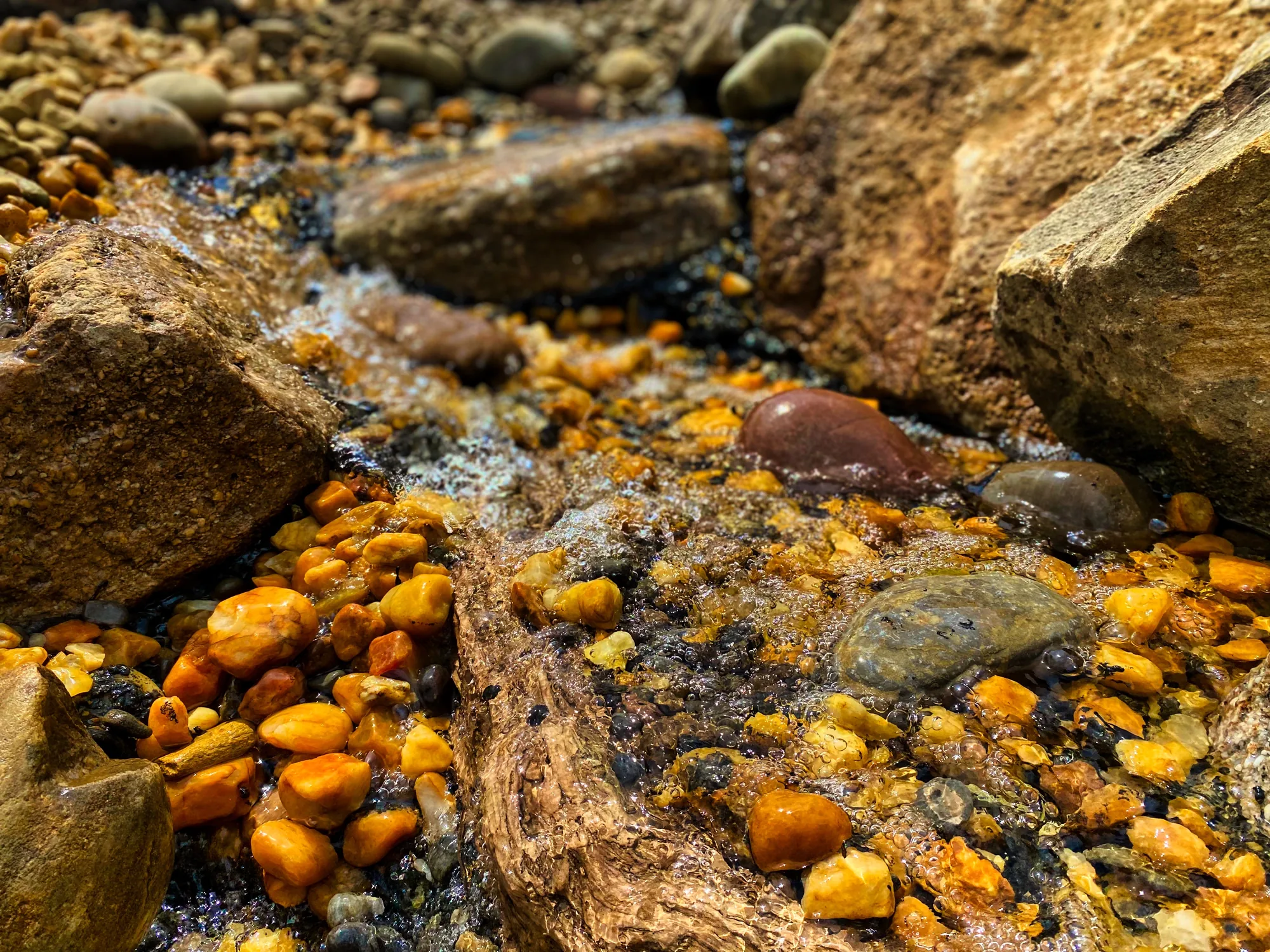 Clear water running over orange and grey pebbles between boulders