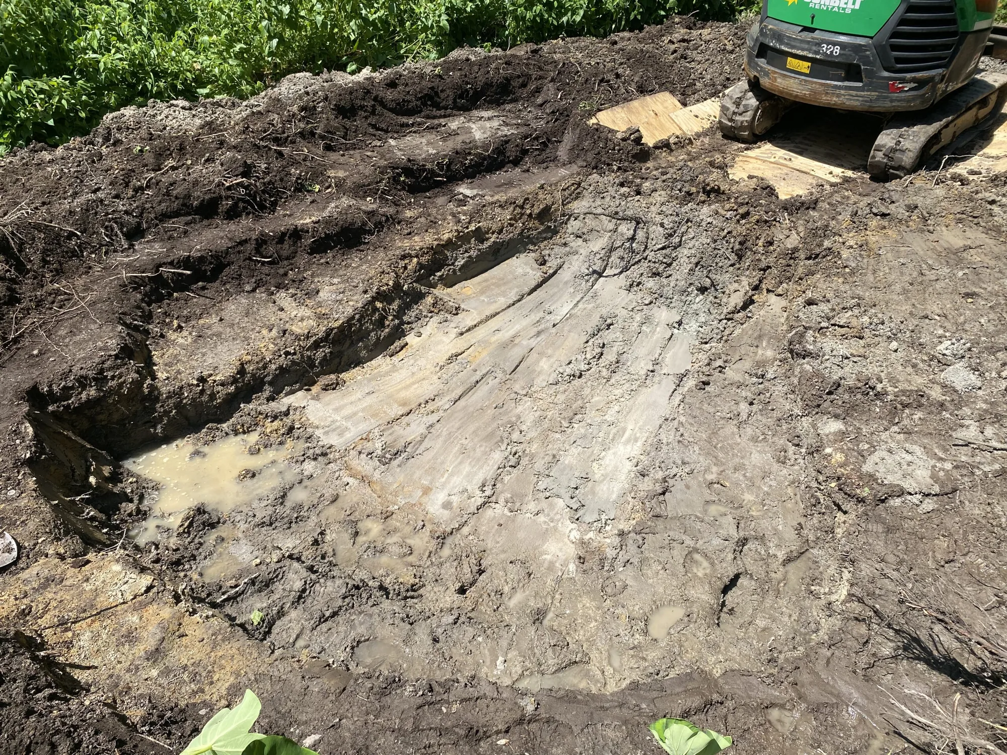 A pond shape dug into a lawn, with a mini excavator parked behind the spoil