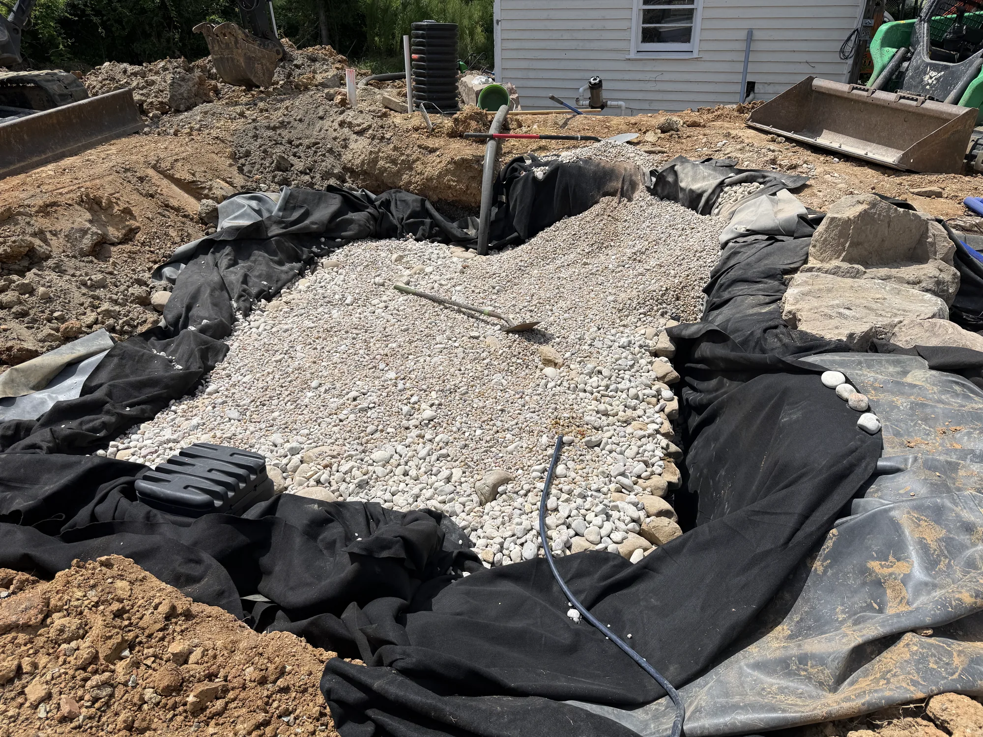 Rubber liner and the first gravel laid in a pond under construction beside a white house