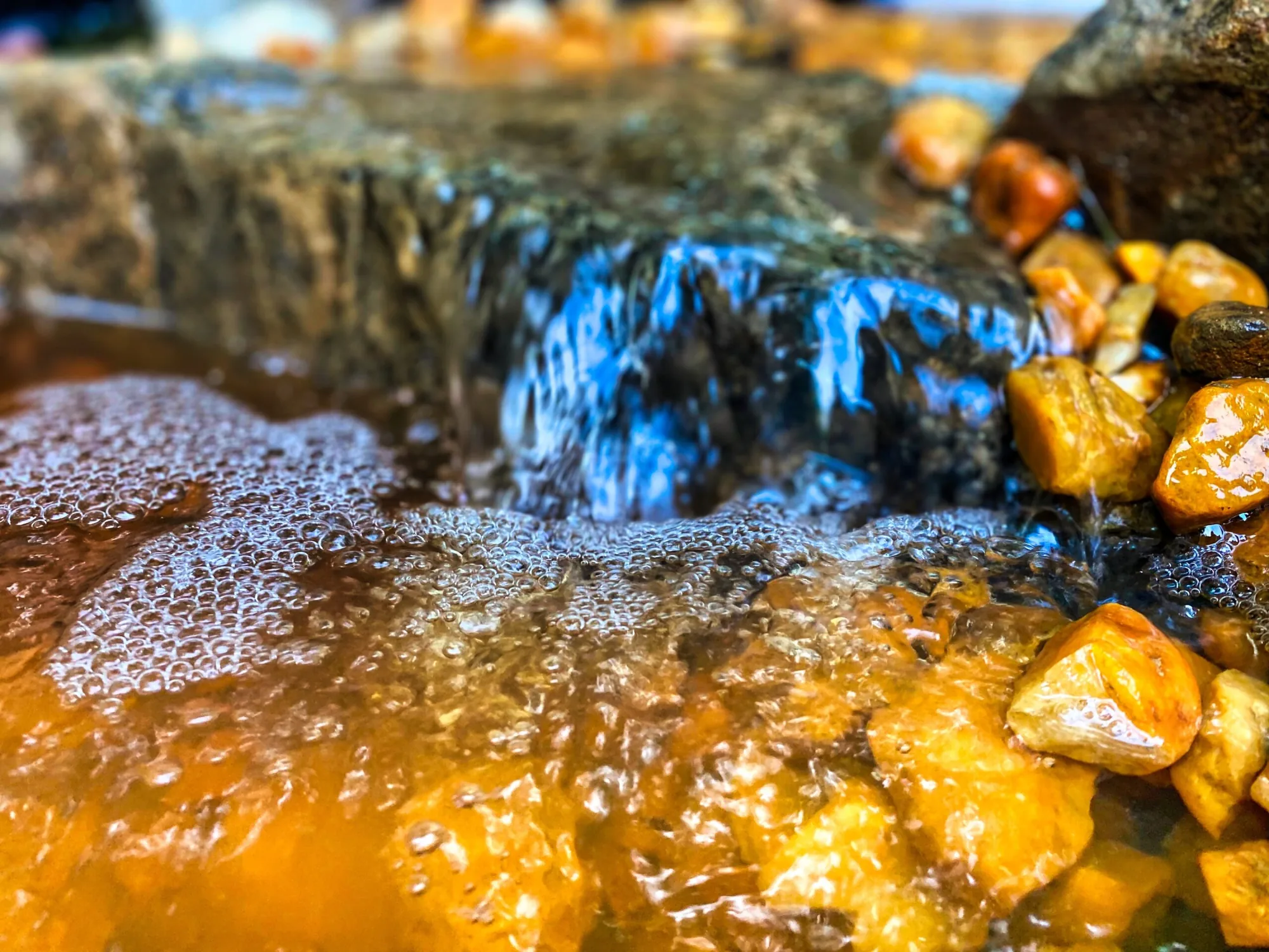 A waterfall pouring over a stone ledge into a pool of amber pebbles