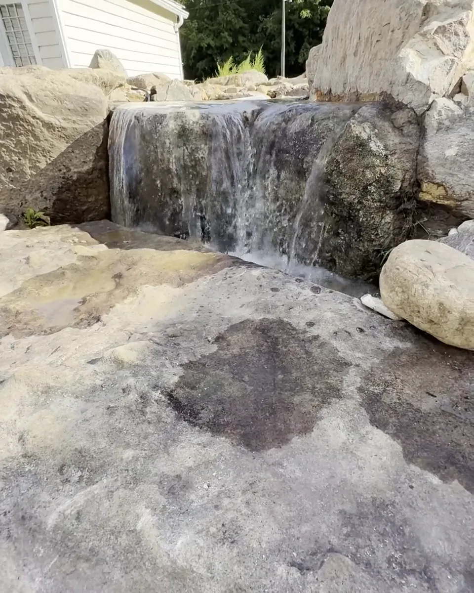 A waterfall spilling over a boulder ledge beside a white house