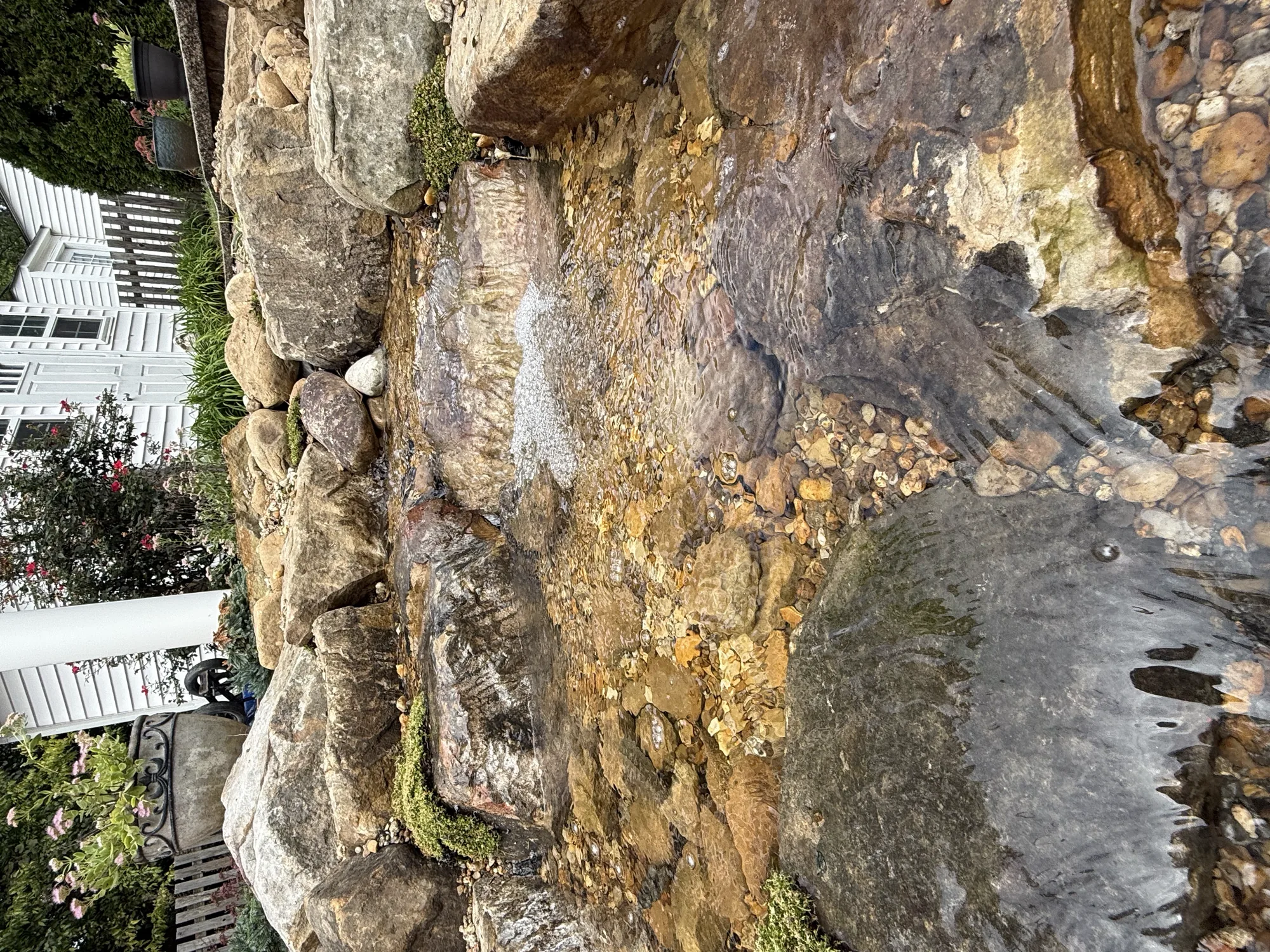 A waterfall stepping down stacked stone beside a white house