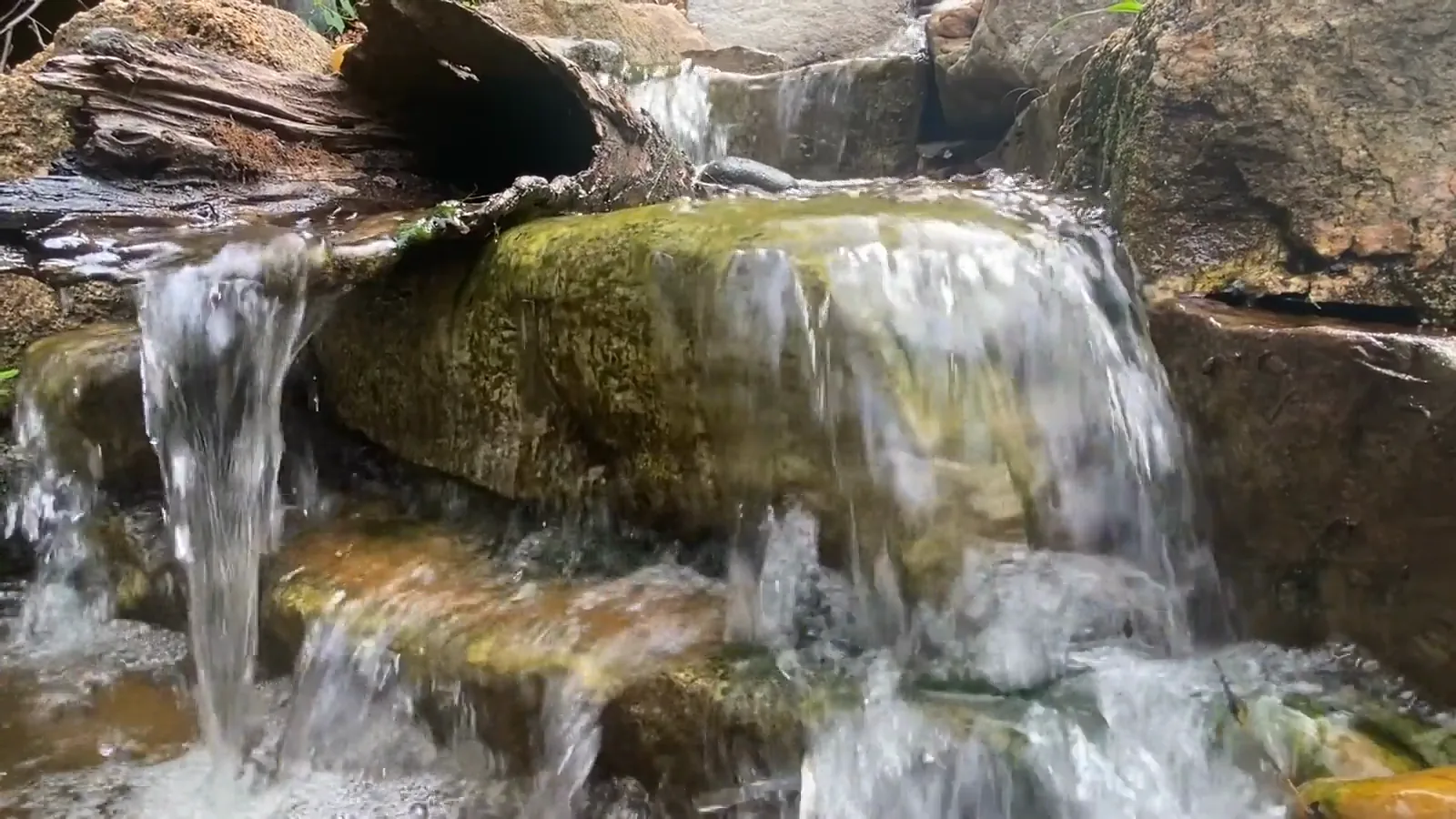 Water spilling over a moss-covered ledge into a shallow pool