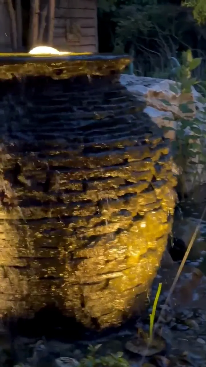A stacked slate urn fountain lit at night