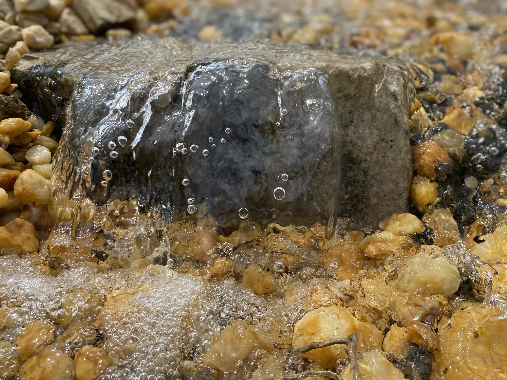 A sheet of clear water sliding over a flat stone, with bubbles caught at the edge