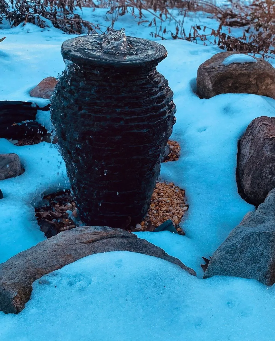 A stacked slate urn fountain still running among boulders in deep snow